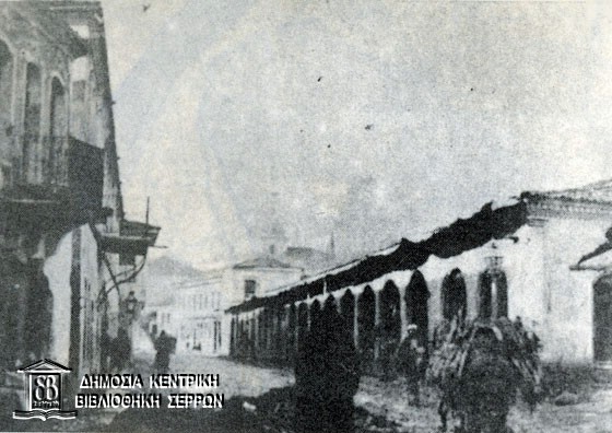 Εικ. 1: Η μακρά αγορά (Ουζούν Τσαρσί). Την προσωνυμία της φαίνεται πως την πήρε από το επίμηκες ισόγειο κτίριο δεξιά, κτισμένο με σχέδιο μετά την πυρκαγιά τον 1849 και πριν από την καταστροφή τον 1913. Στο βάθος, πίσω από το κτίριο, διακρίνεται αχνά ο μιναρές τον Εσκί Τζαμί. (Πηγή: Ε.Η.  Ayverdi, βλ. σημ. 6).